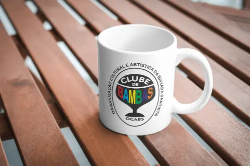 Logotipo da OCABS estilizado em uma caneca vetorizada projetada sobre uma mesa real.