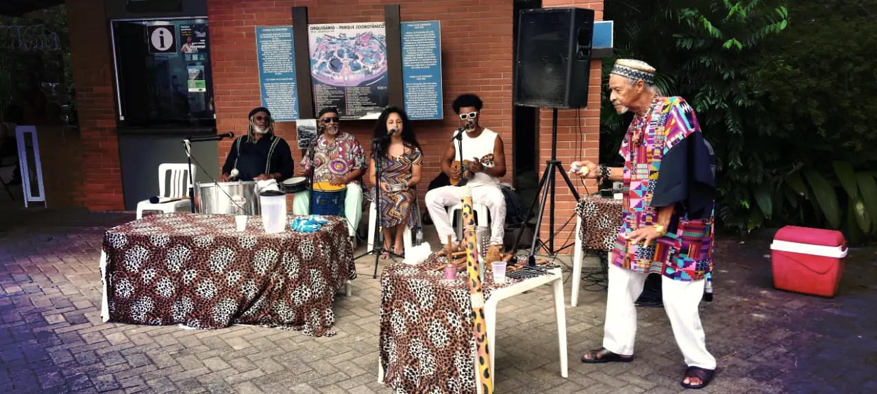 Artista se apresentando ao vivo com grupo musical ao fundo.